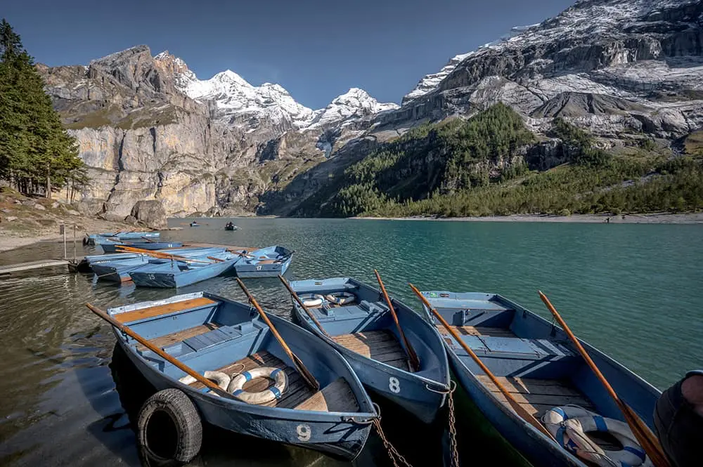 Blue rowboats for hire moored at the dock of Oeschinensee with snow-capped BlĂĽemlisalp peaks reflected in the turquoise water, Kandersteg Switzerland