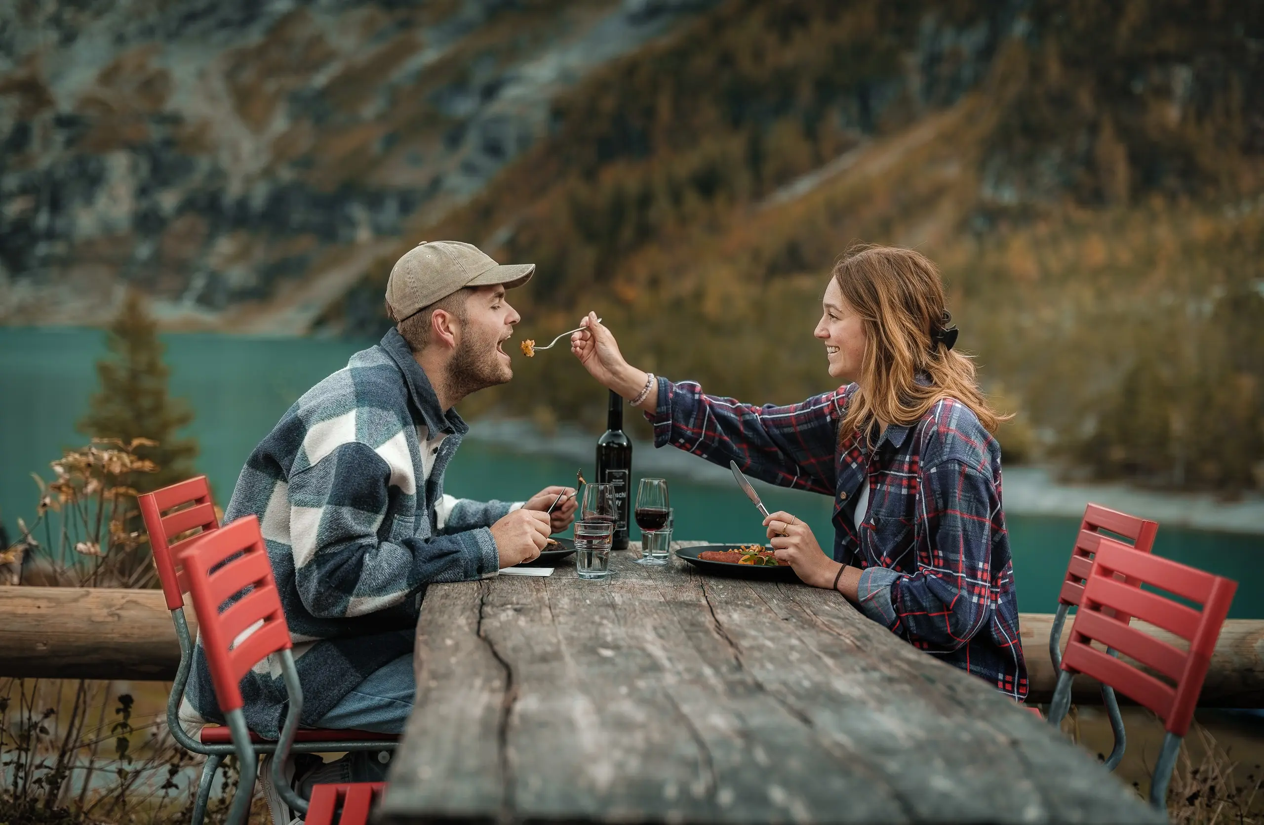 Couple dining on the terrace of Restaurant Oeschinensee with red wine and a view of the turquoise lake and autumn alpine landscape, Kandersteg Switzerland