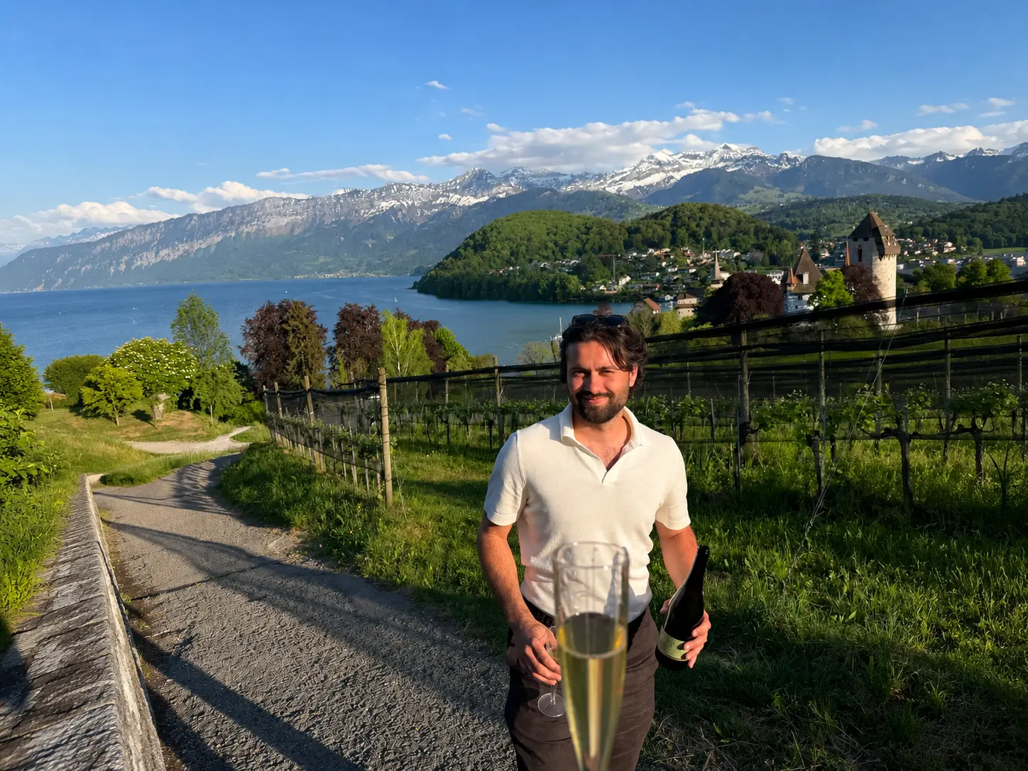 Local guide holding white wine in Spiez vineyard above Lake Thun with medieval castle and Bernese Alps, summer Switzerland