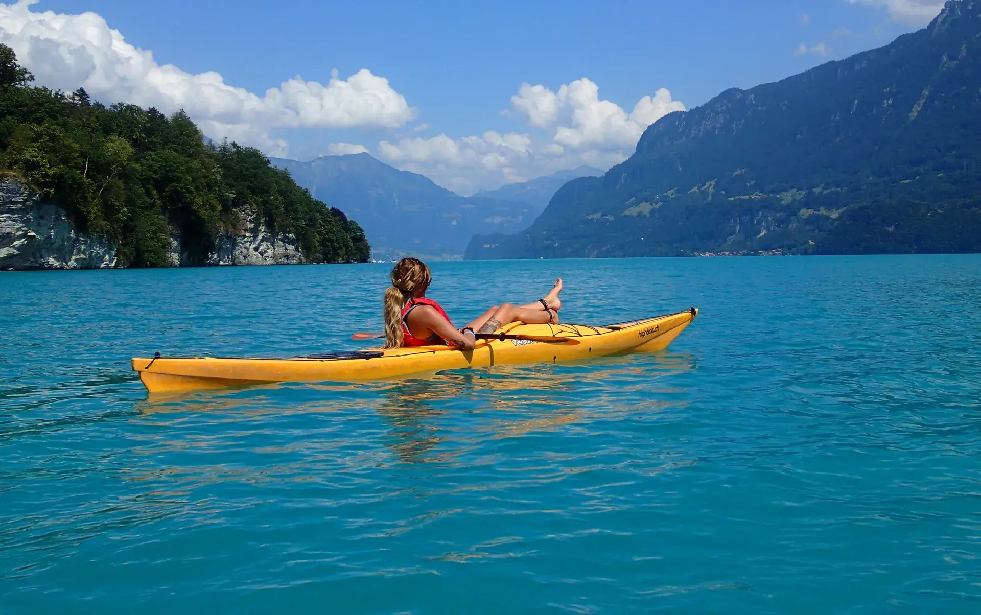Woman relaxing on yellow kayak on turquoise Lake Brienz, summer kayaking near Interlaken Bernese Oberland Switzerland