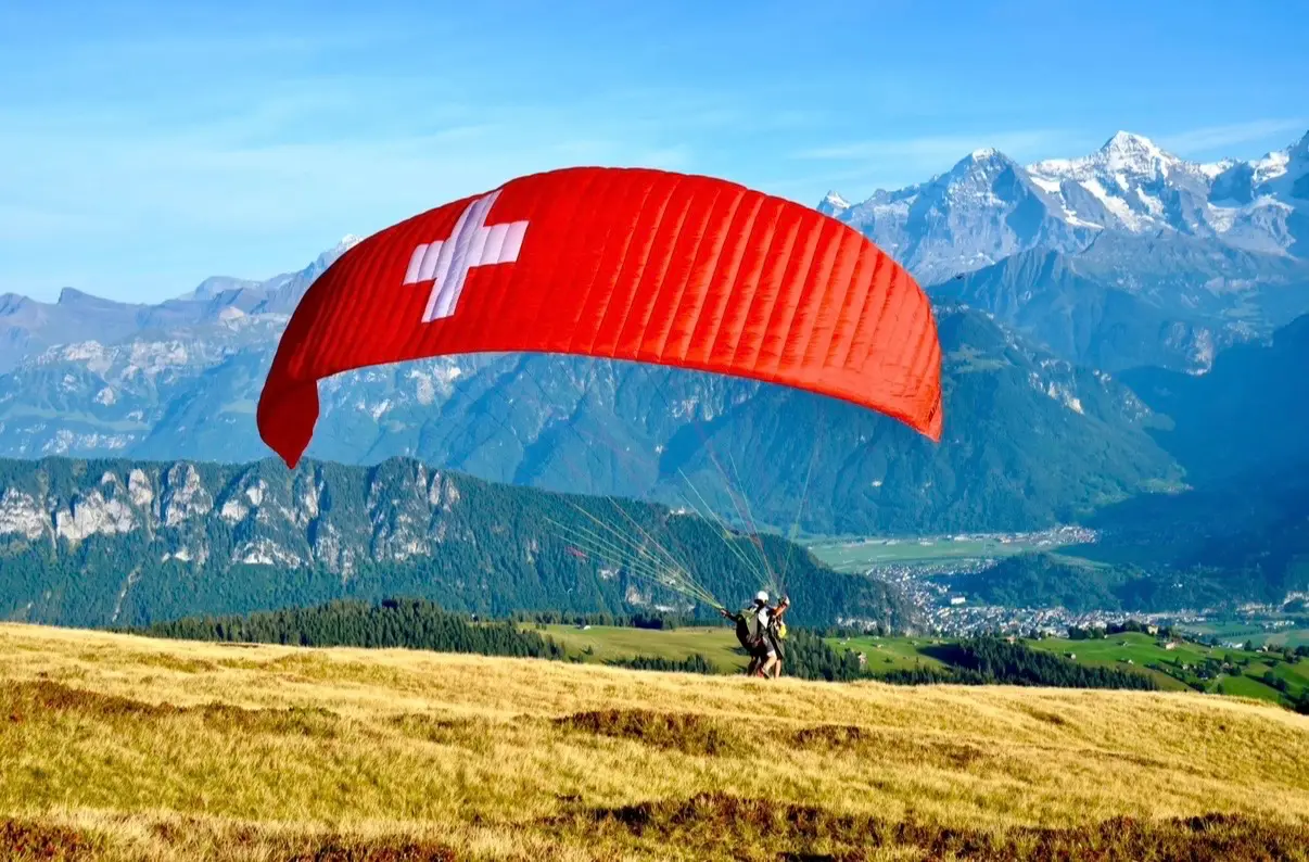 Tandem paragliding takeoff with Swiss flag canopy above Interlaken valley and Jungfrau massif, Bernese Oberland