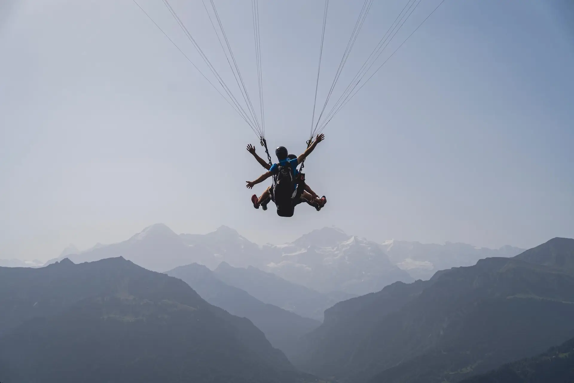 Tandem paragliding passenger with arms wide open above the Swiss Alps near Interlaken, Bernese Oberland valley below