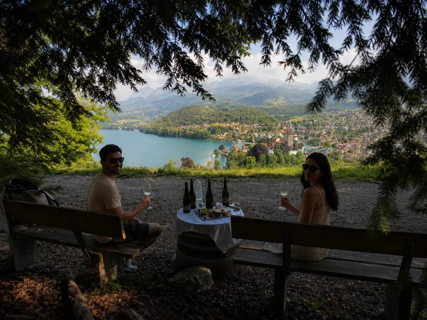 Couple on vineyard benches with white wine above Lake Thun and Spiez castle, intimate small-group wine tasting Switzerland