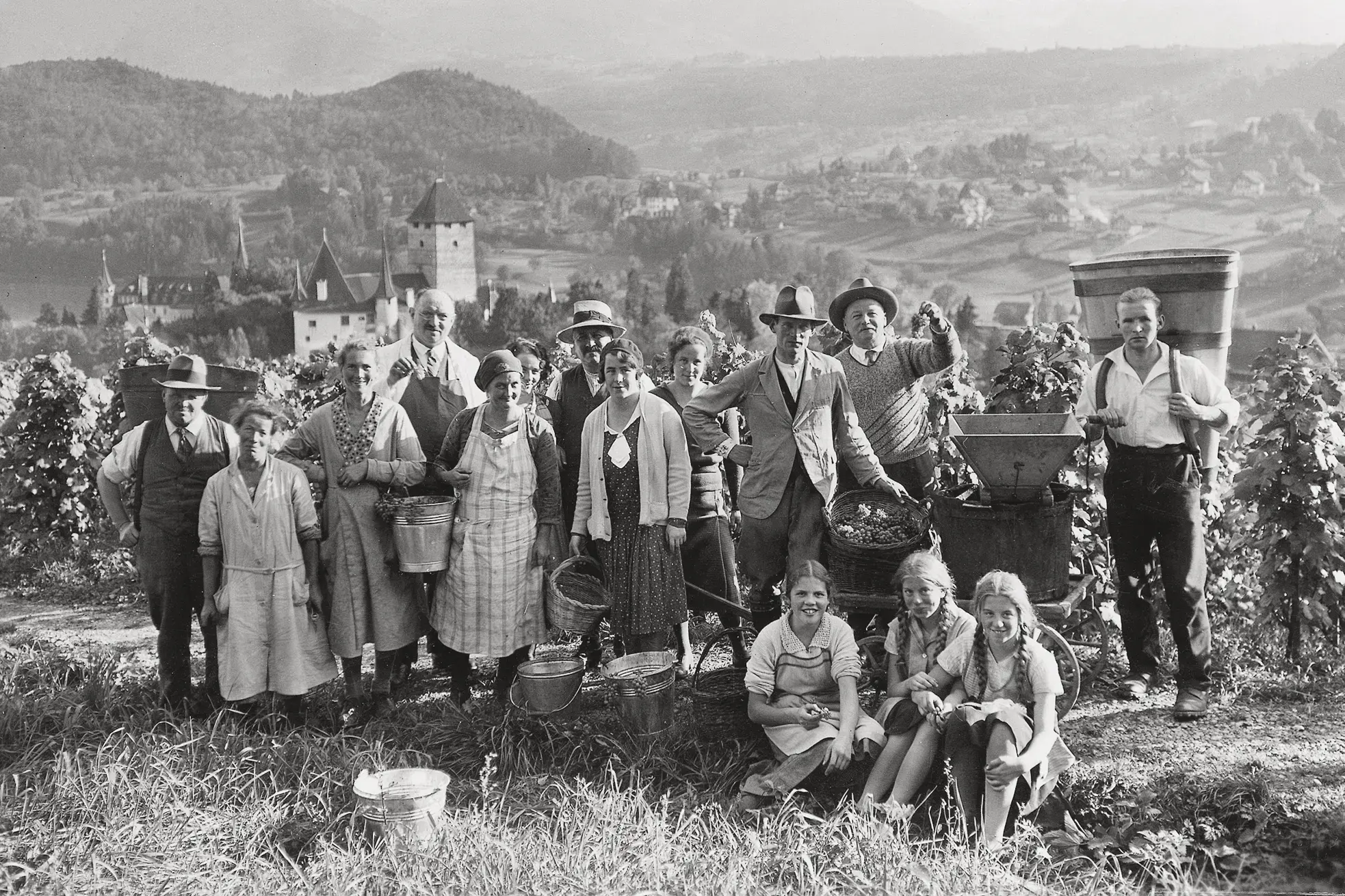 Historical grape harvest team in Spiez vineyard above Schloss Spiez castle with wicker baskets, traditional Swiss winemaking