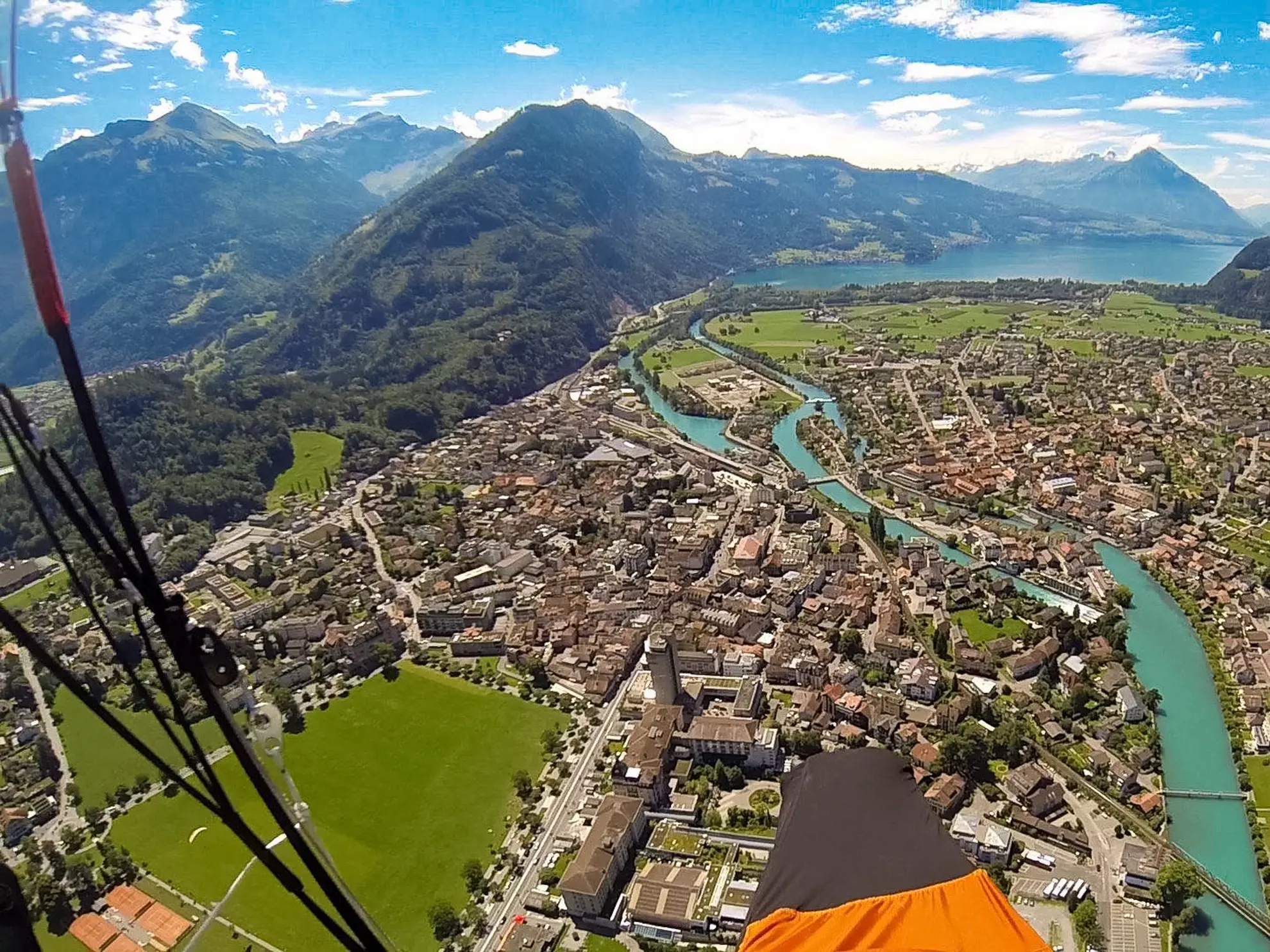 Aerial paraglider POV over Interlaken with Höhematte meadow, Aare river and Lake Brienz visible, Switzerland