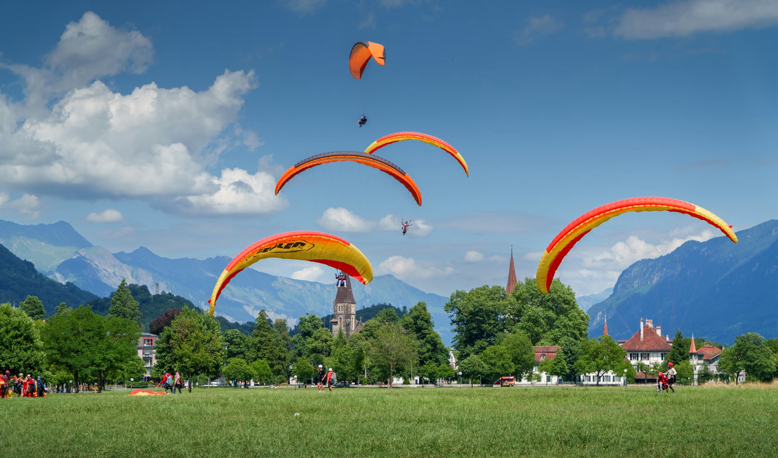 Multiple paragliders landing on Höhematte meadow in Interlaken town centre with alpine mountains behind Switzerland