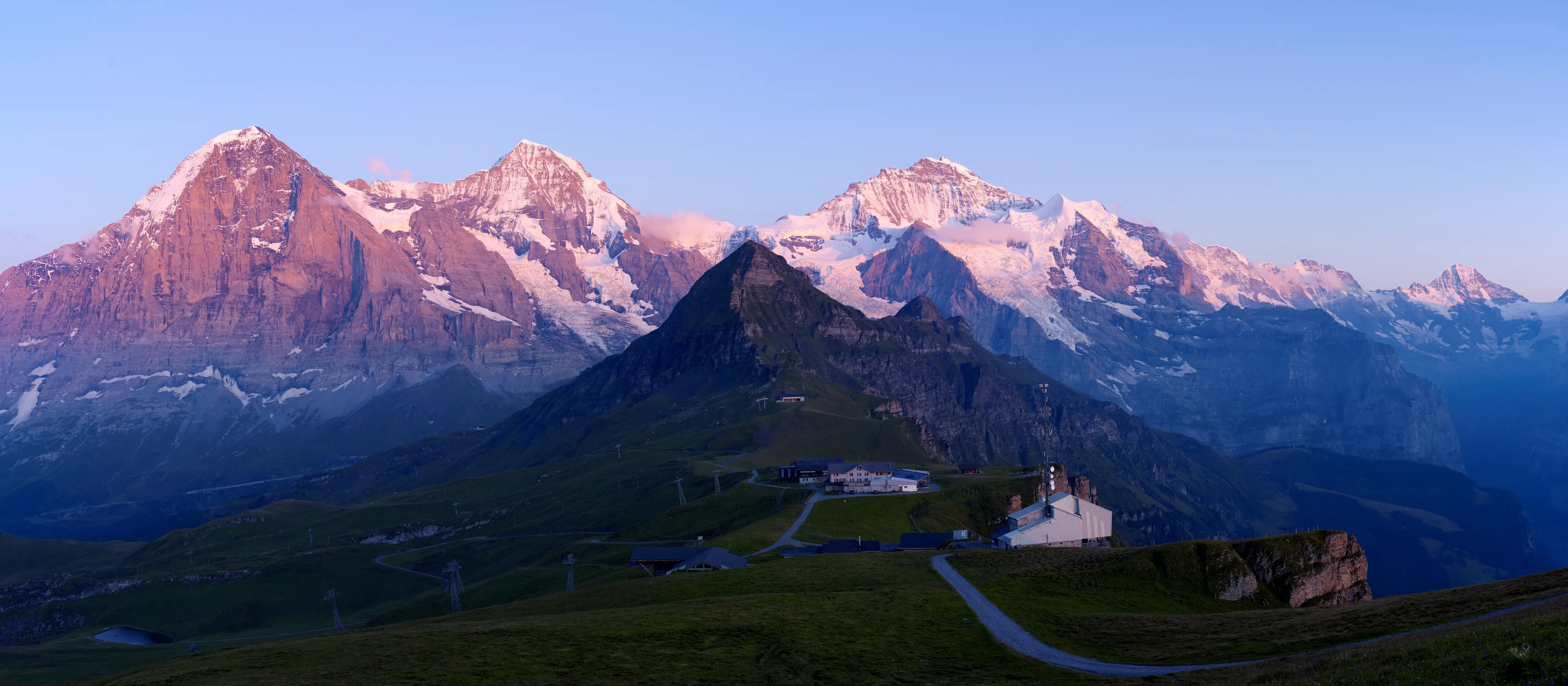 Eiger Mönch and Jungfrau peaks glowing pink at sunrise seen from Männlichen above Grindelwald Bernese Oberland Switzerland