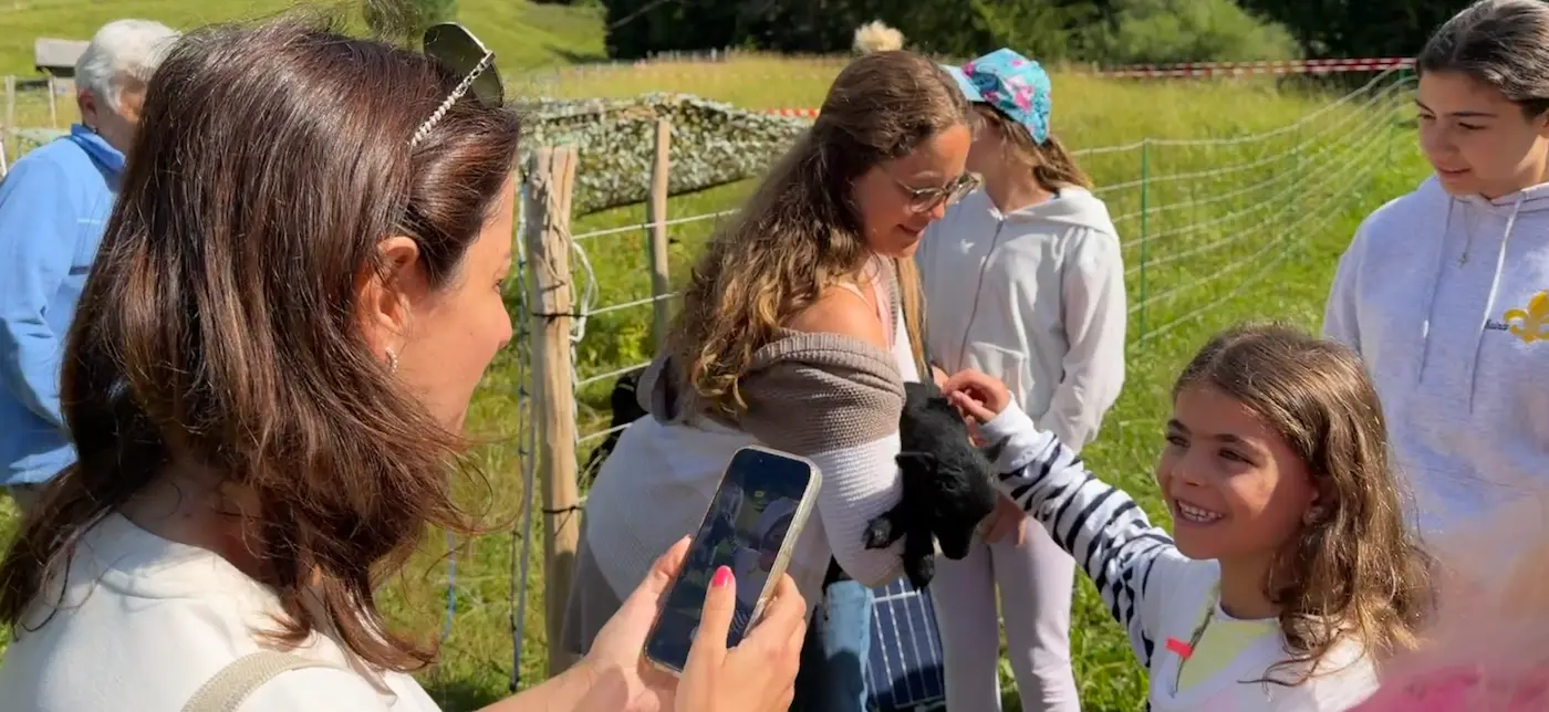 Girl petting a black baby goat while her mum films it on a kid-friendly Swiss farm tour near Interlaken