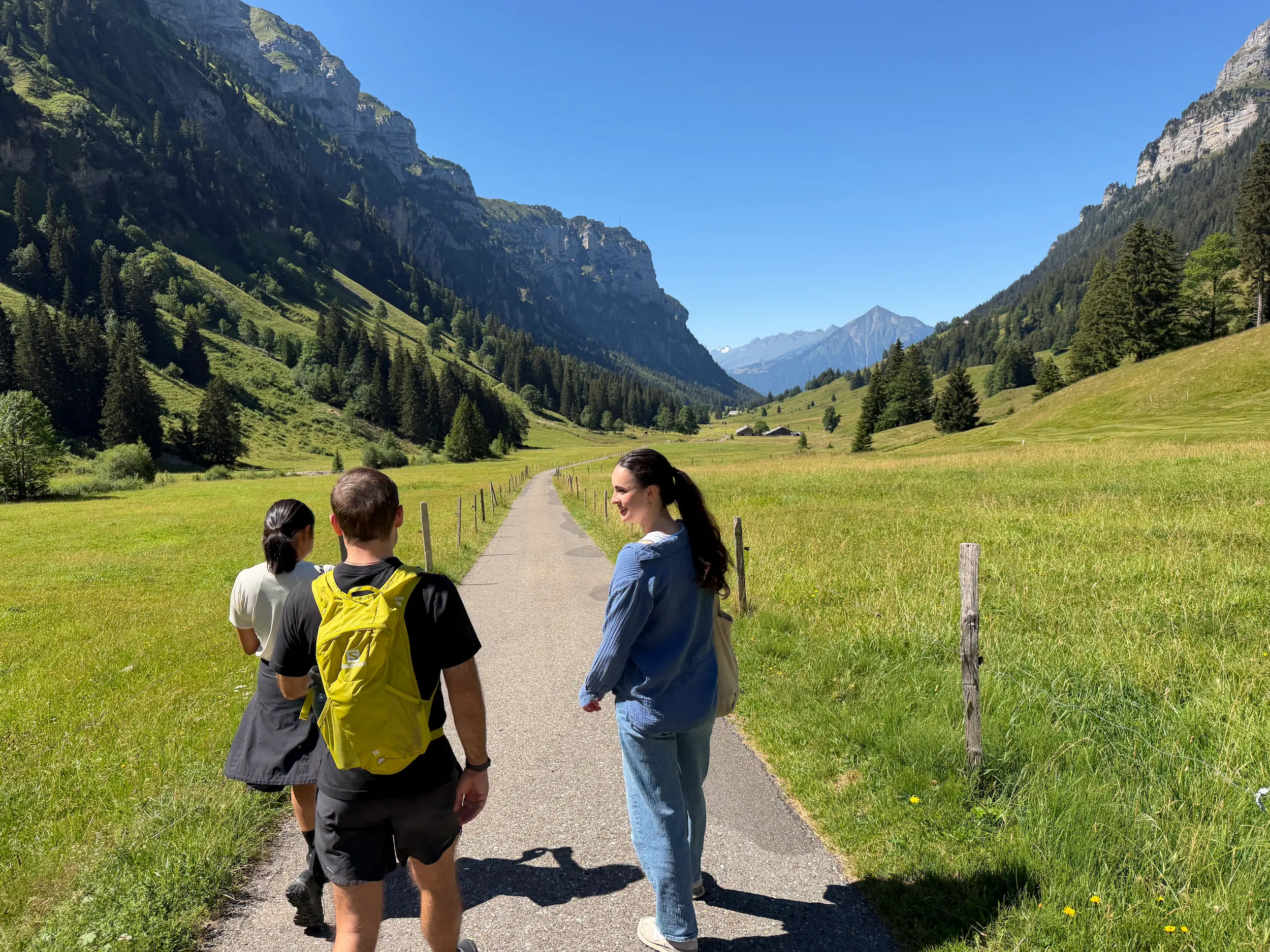 Three travellers walking along the valley path in the Justistal, Bernese Oberland, between green alpine meadows and steep limestone cliffs