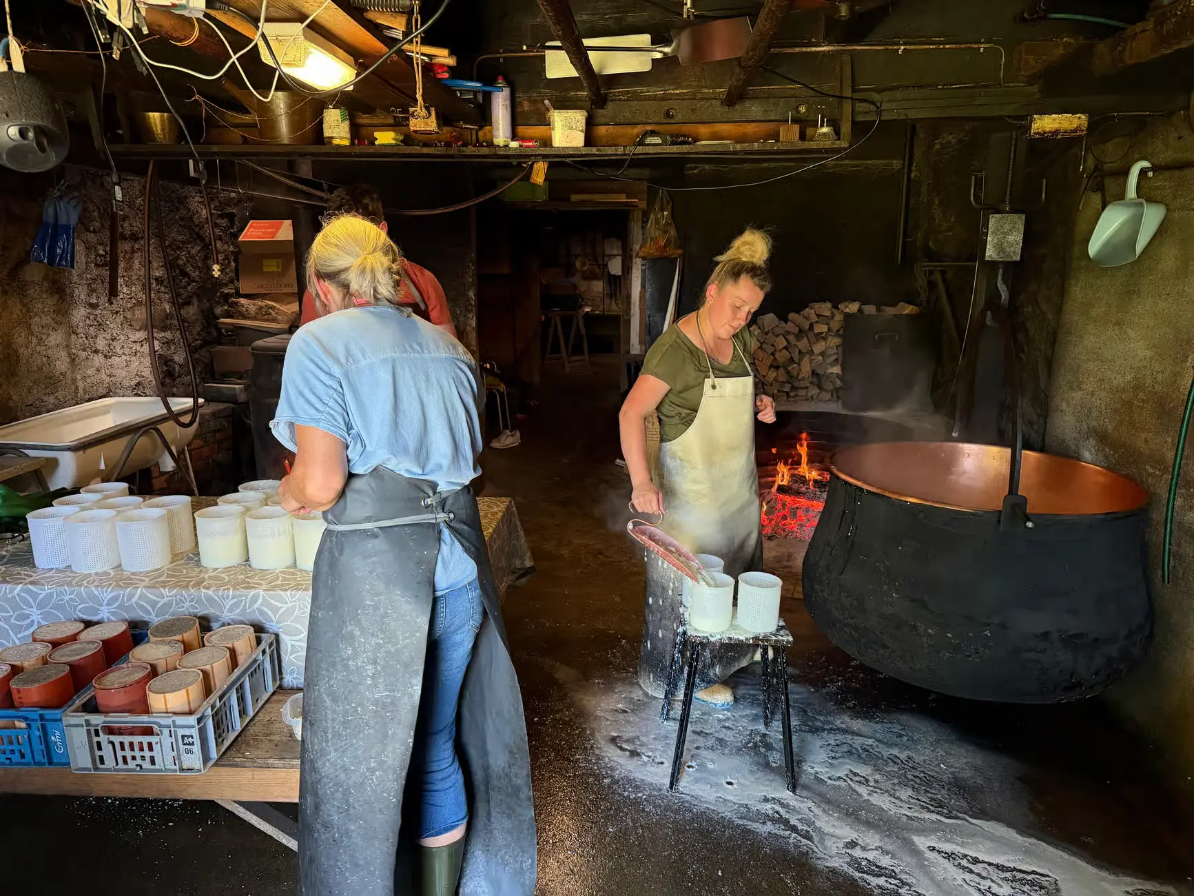 Cheesemakers filling moulds beside a copper cauldron over an open wood fire in the alpine dairy, the traditional way cheese is still made on the farm