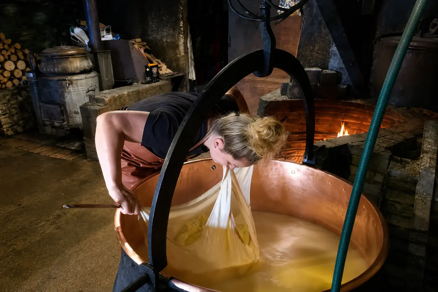 Cheesemaker lifting the curd from a copper cauldron over a wood fire on a Swiss alp, how Chästeilet wheels are made