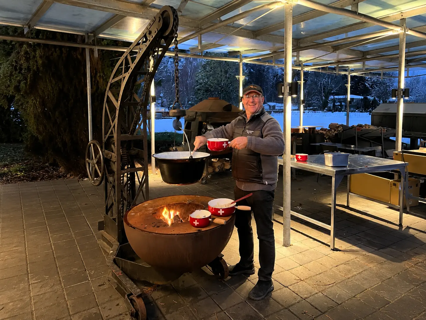 Swiss man preparing fondue in caquelons over an open fire on a winter evening, fondue is a cold season dish